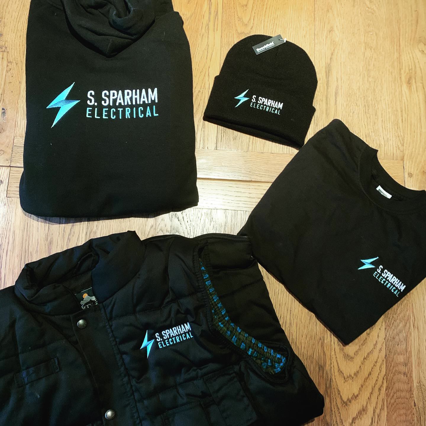 S. Sparham Electrical branded workwear: hoodie, beanie, t-shirt and body warmer, each carrying the lightning bolt mark