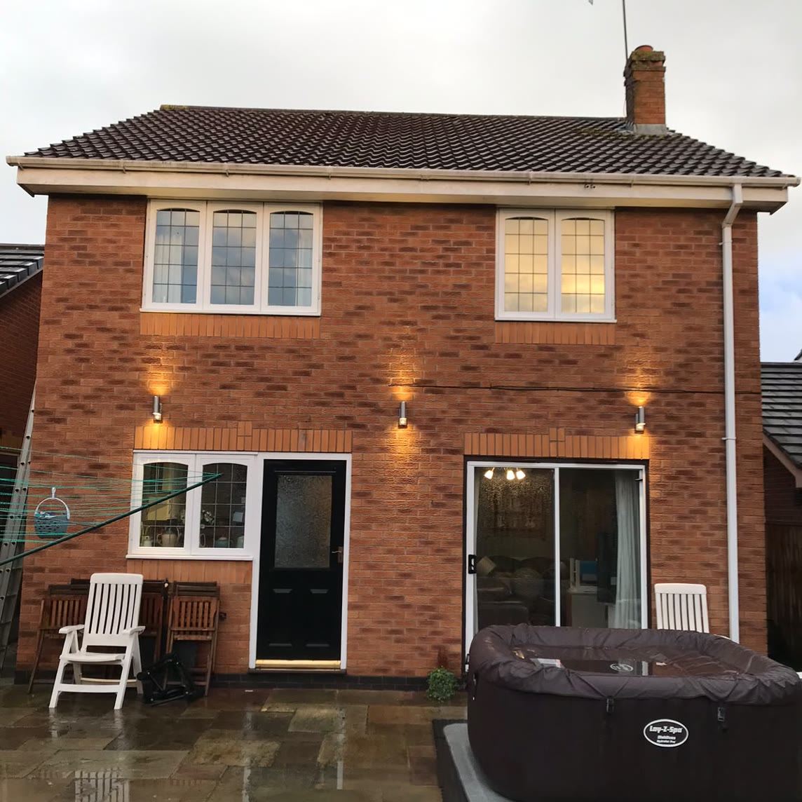The same elevation at dusk, with three up-and-down wall lights throwing light up the brickwork and down over the patio below