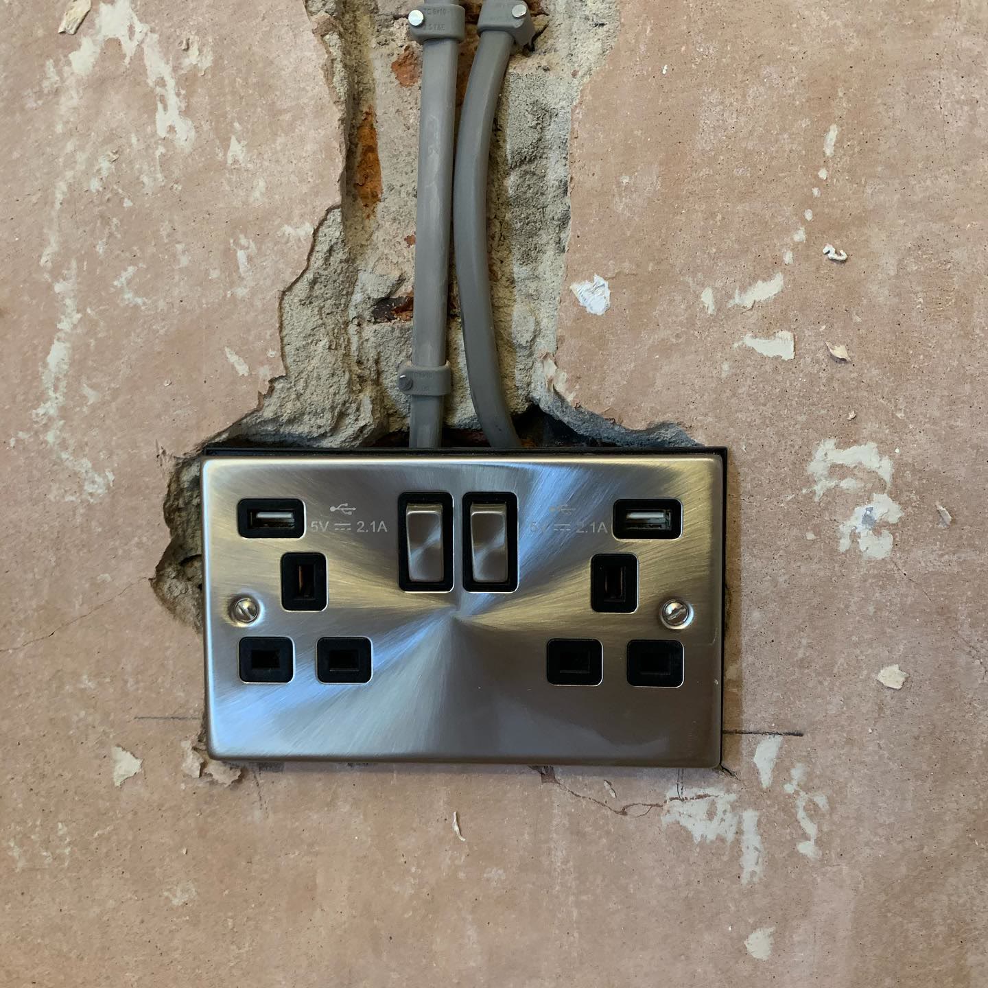 Brushed steel double socket with USB charging, newly installed and chased into a bare plaster wall
