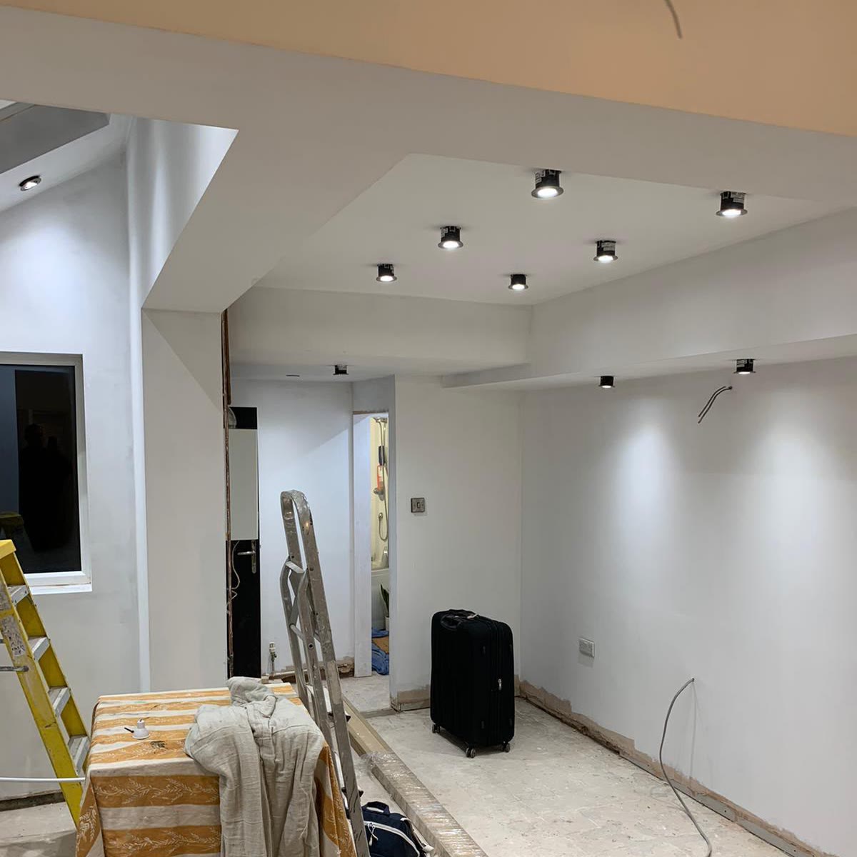 Black surface-mounted spotlights installed across a newly plastered ceiling in an open-plan room, lit and working before the room is decorated