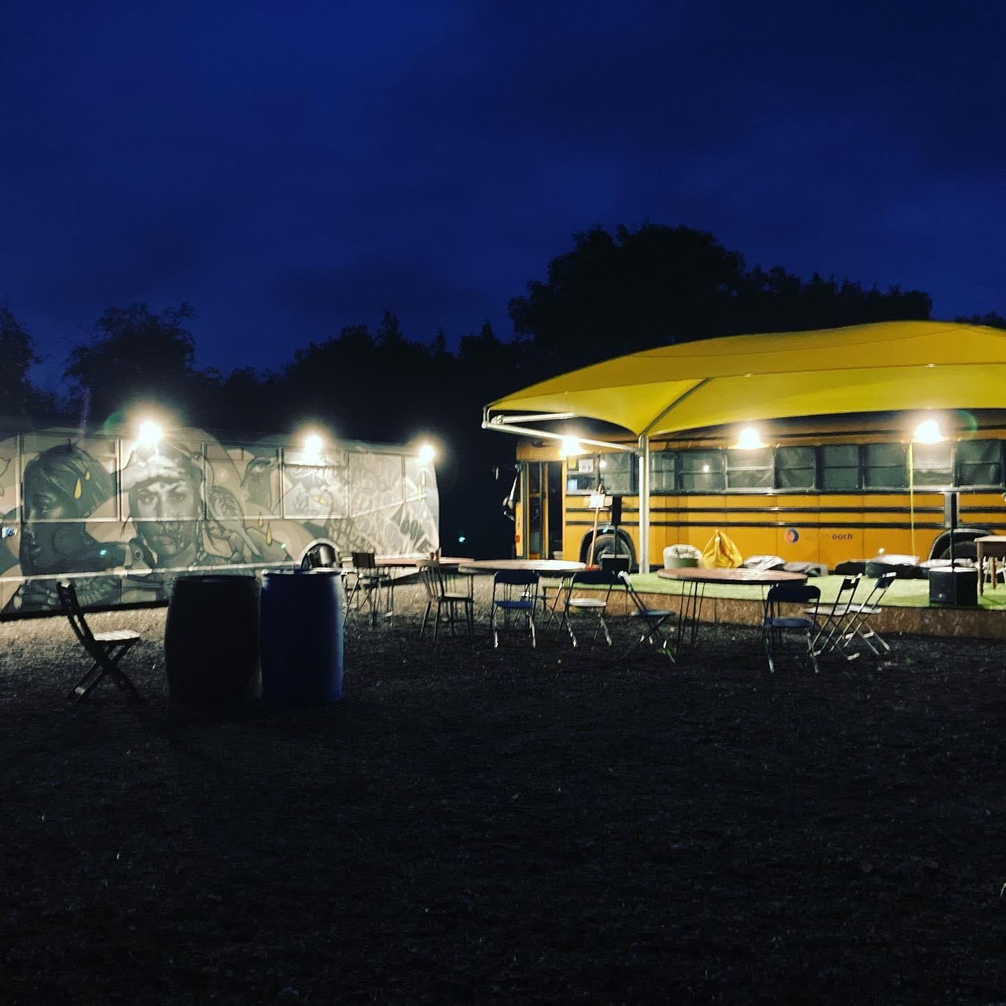 Outdoor lighting at dusk over a catering unit and seating area, with lamps along the canopy and the serving hatch lit