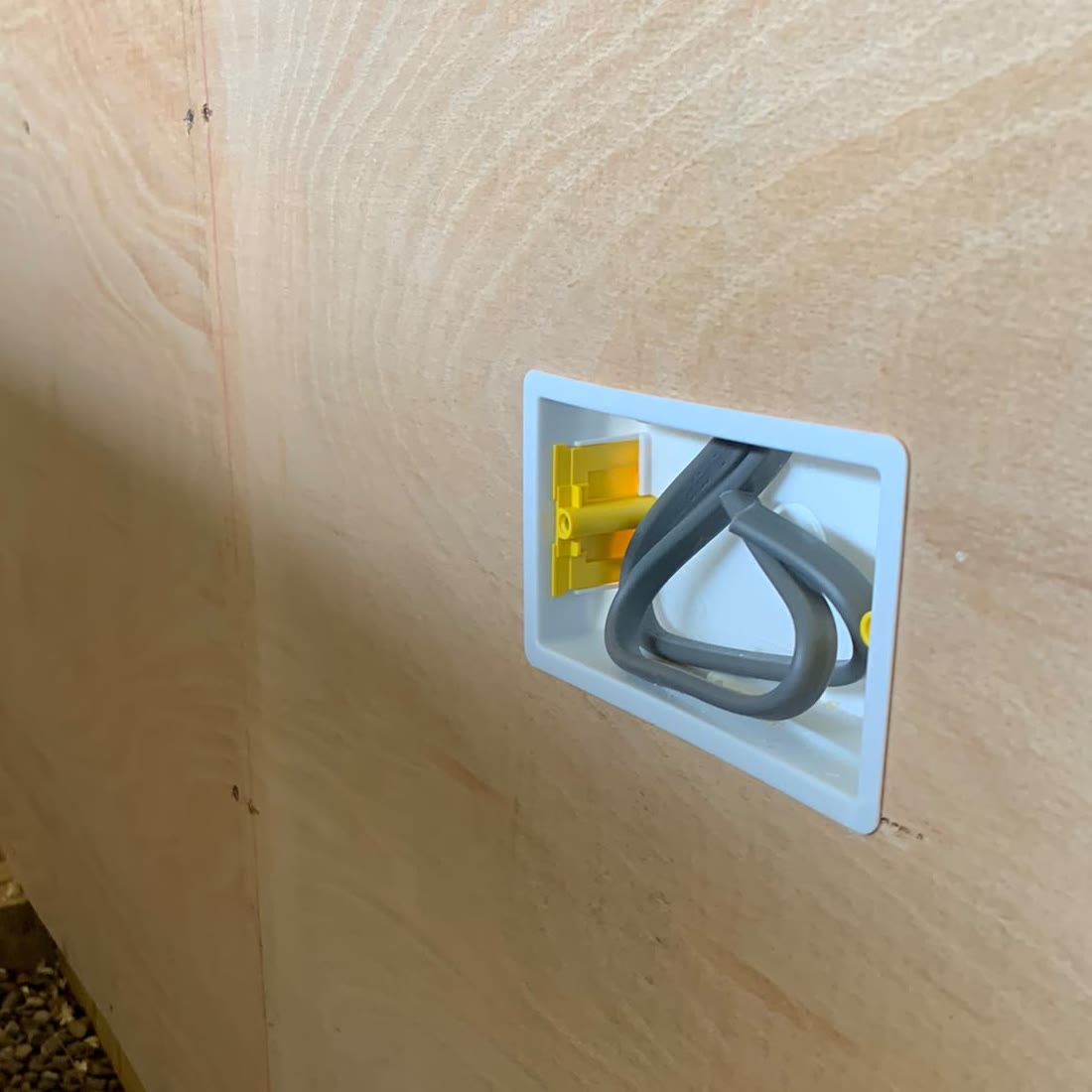 Weatherproof outdoor socket recessed into a plywood-lined wall, with the cable coiled ready for second fix