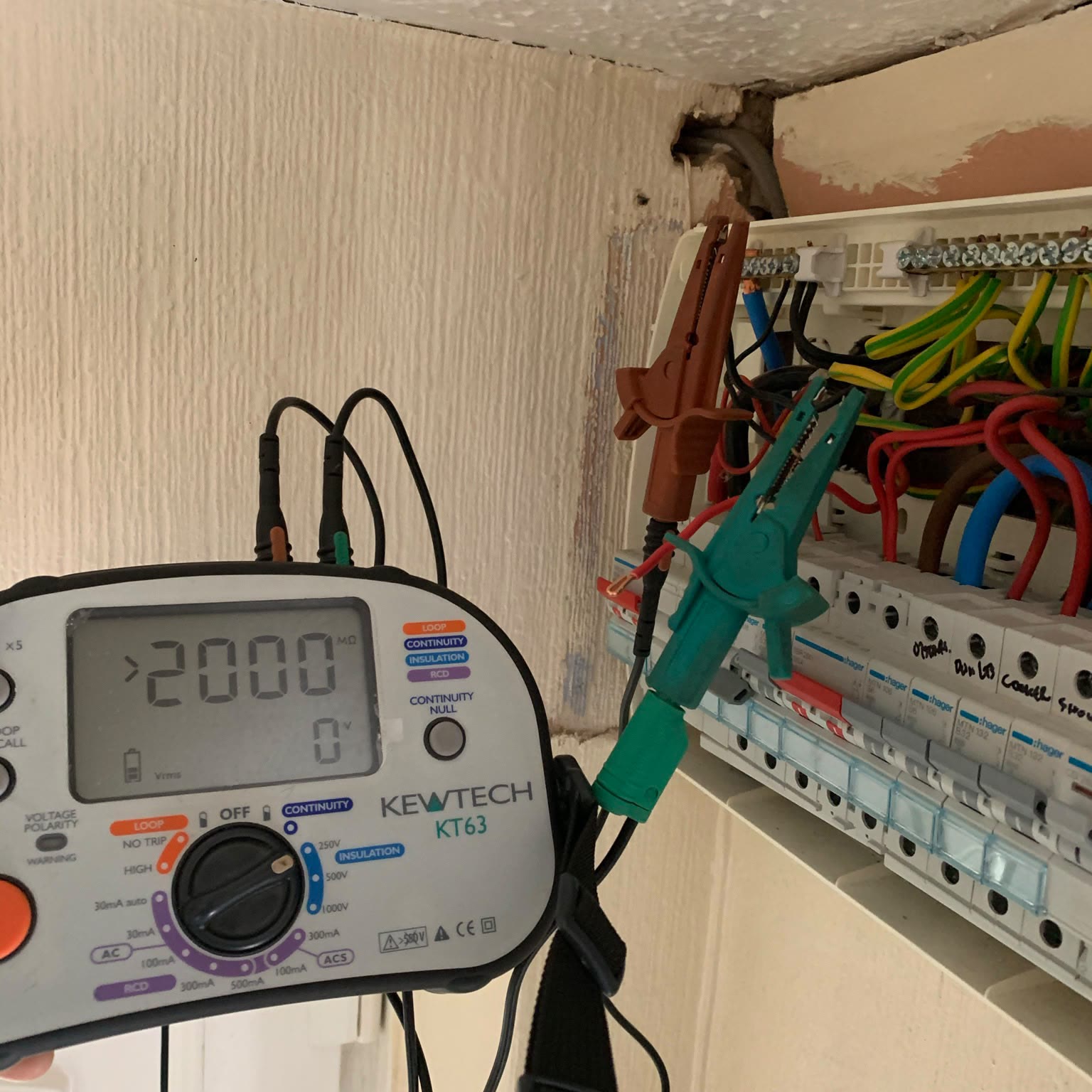 Testing in progress at a consumer unit, with a Kewtech multifunction tester clipped to the circuit conductors