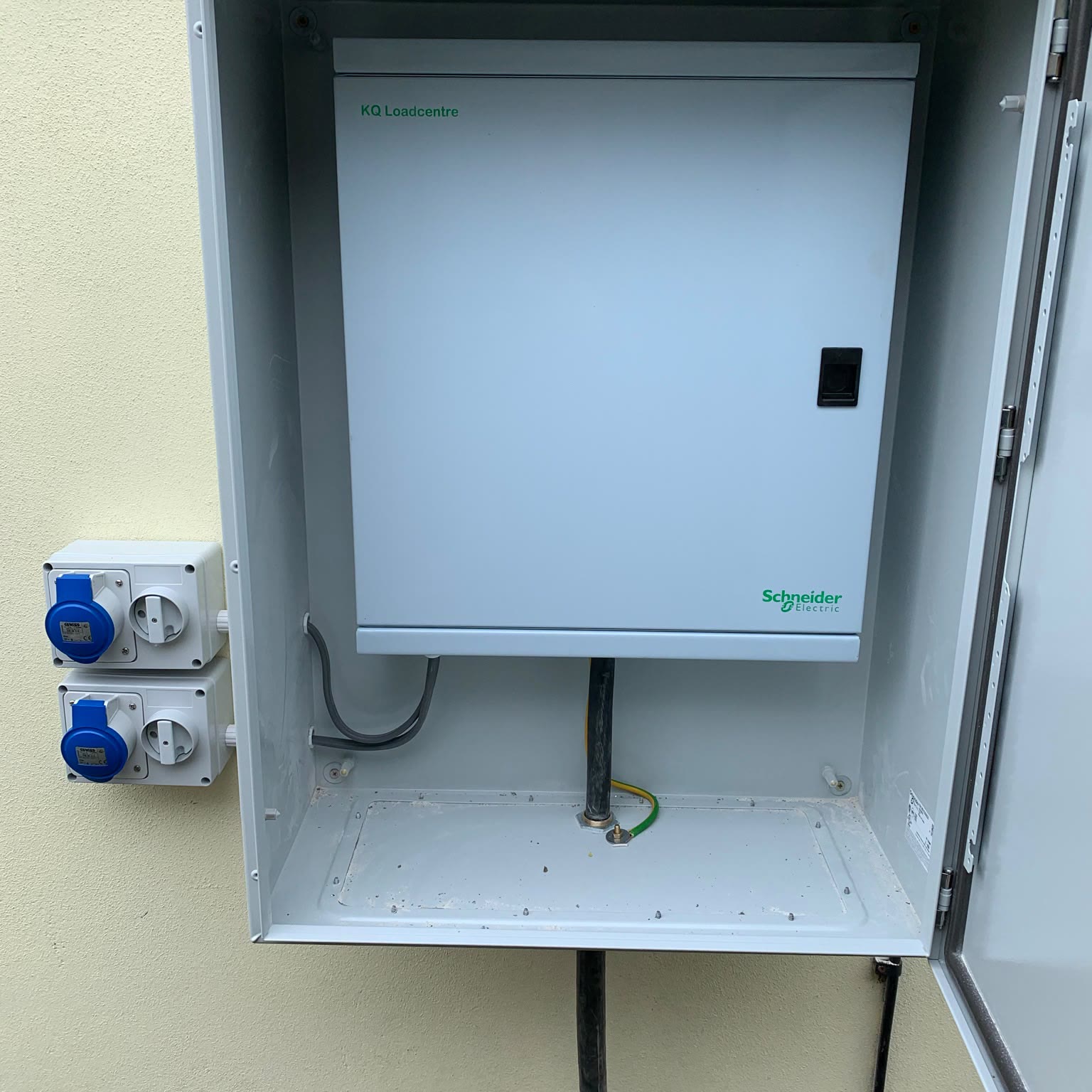 Outdoor distribution board in a lockable steel enclosure, with two industrial blue sockets mounted on the wall beside it