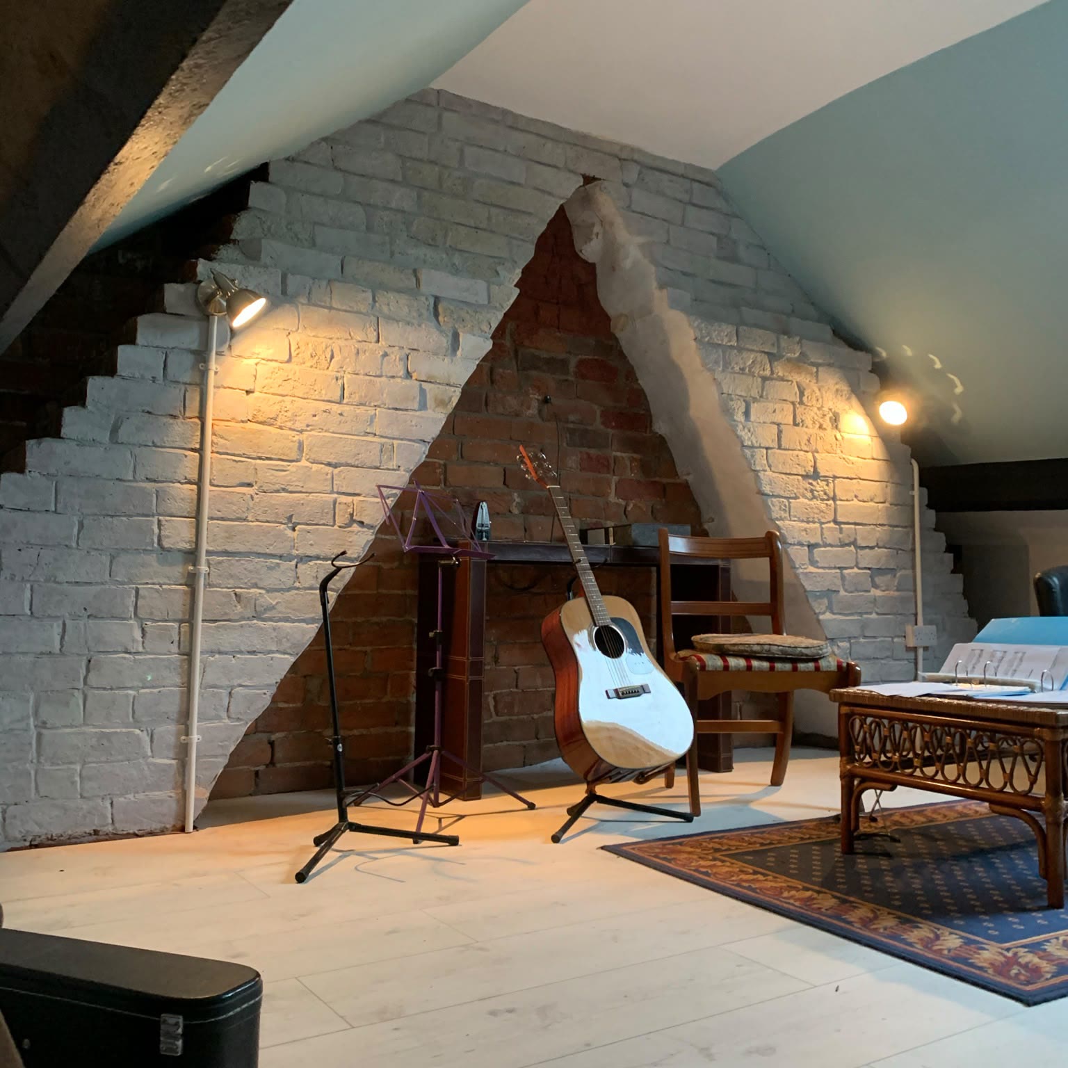 Converted loft room with white painted brickwork, adjustable wall spotlights and a ceiling light over the exposed chimney breast
