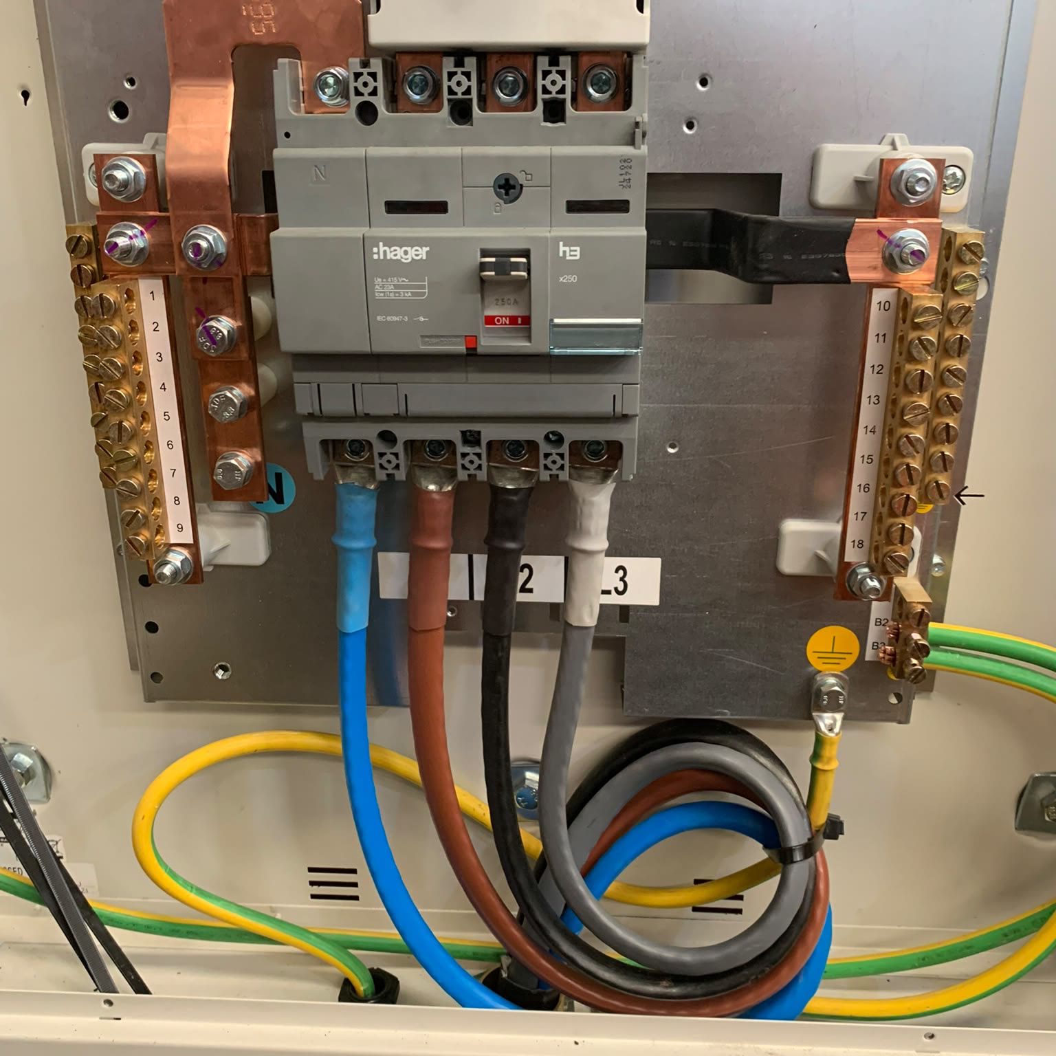 Three-phase switch and busbar inside a distribution board, with the incoming tails and earthing terminated and the ways numbered