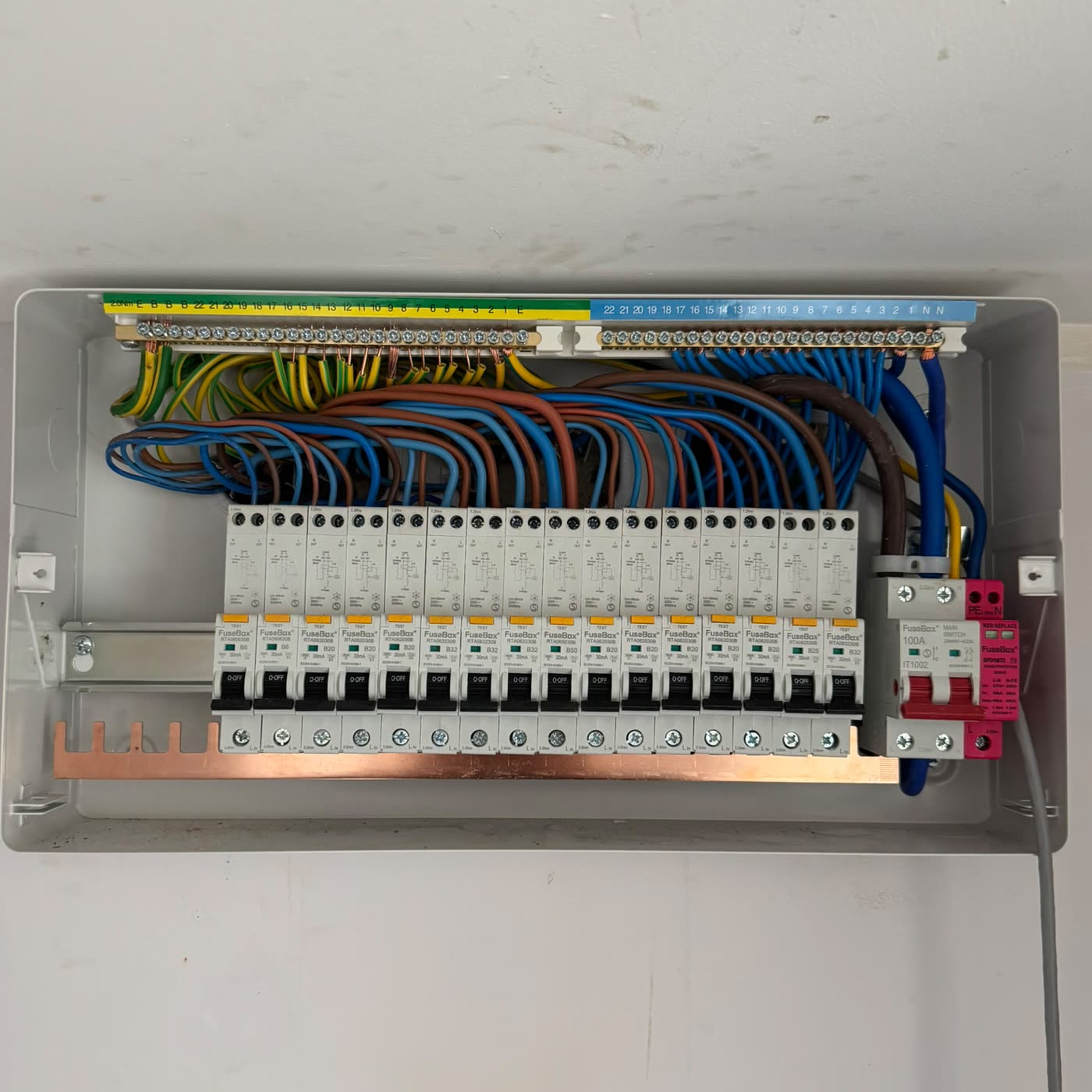 New FuseBox consumer unit with the cover off, fully populated with circuit breakers, a 100 amp main switch and a surge protection device, and every circuit cable terminated