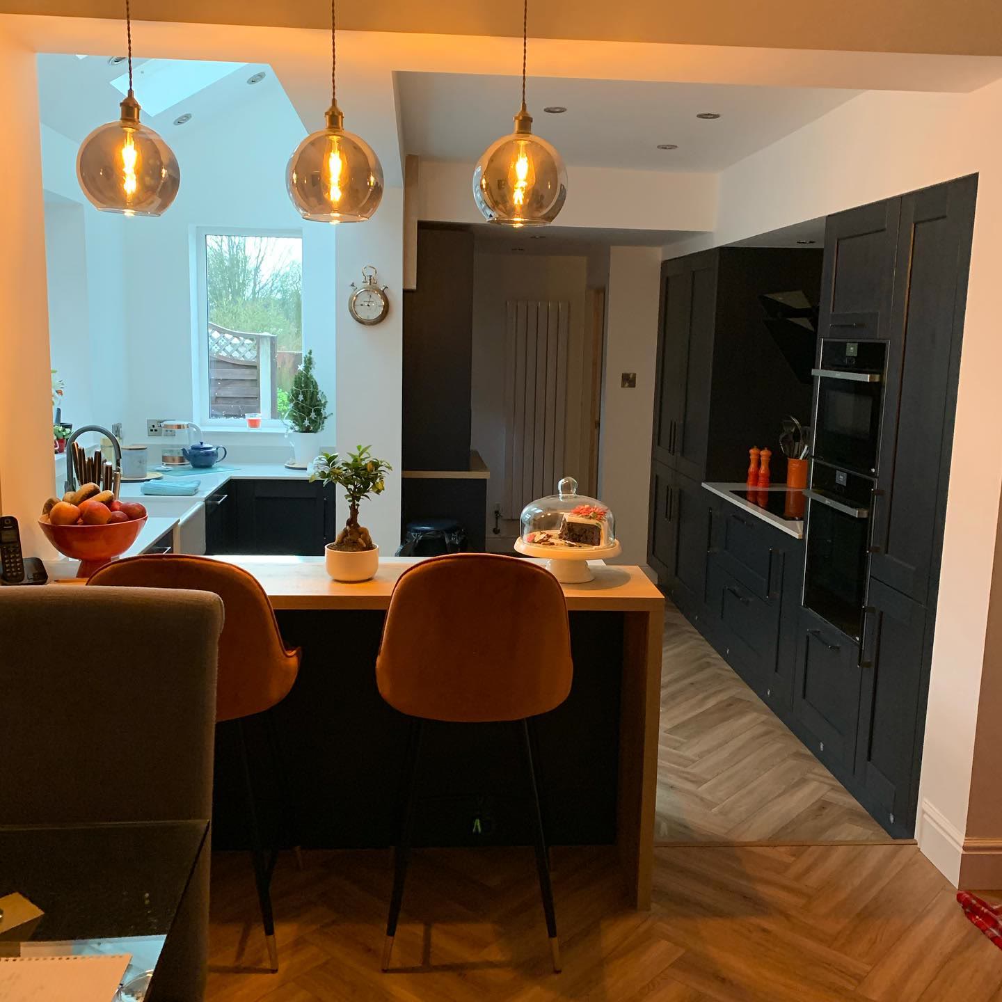 Open-plan kitchen and dining space with three glass pendant lights over the island and downlights beyond