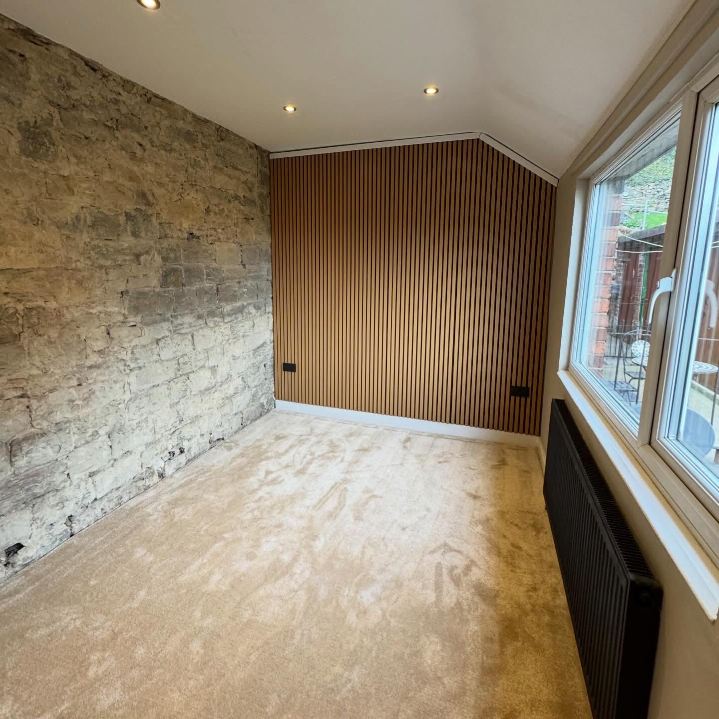 Renovated room with recessed downlights, exposed stone wall and a slatted oak feature wall with flush sockets
