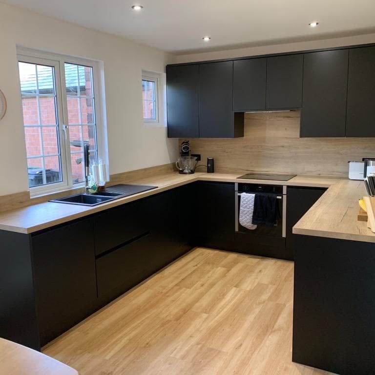 Finished kitchen in matt black with a wood-effect worktop, downlights set through the ceiling and lighting under the wall units